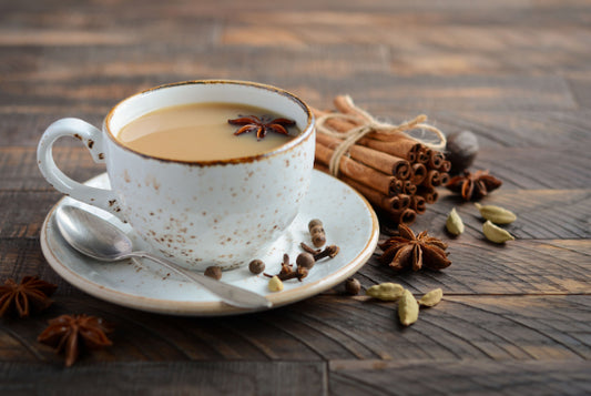 Chai tea in a cup and saucer with herbs on a wooden background