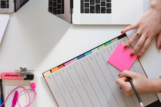 Woman writing on a sticky note on top of calendar and next to laptop