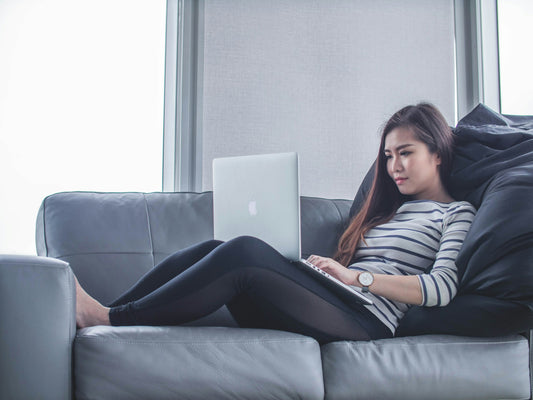 Woman sitting on sofa researching adaptogens on MacBook Pro